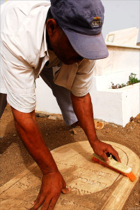 Cleaning dirt off Hebrew letters of Jewish tombstone